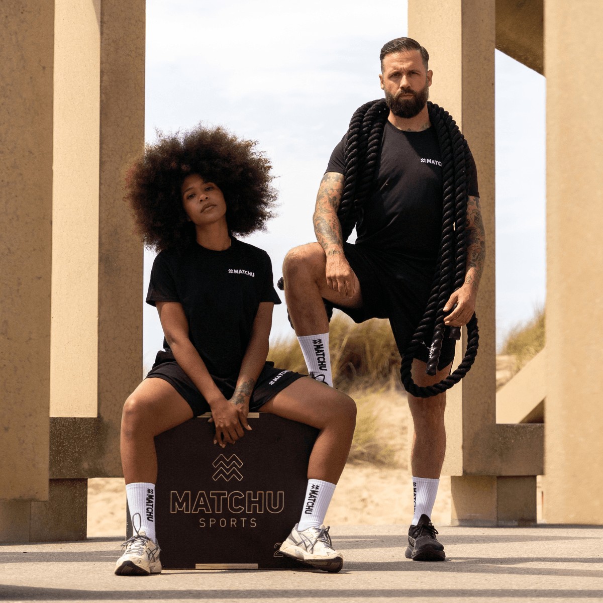 Two athletes in MATCHU kit in the dunes, one on a plyo box, one with a battle rope